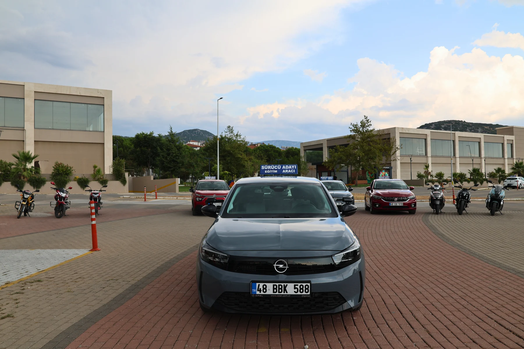 A gray Opel and other Şah Driving School training vehicles behind it